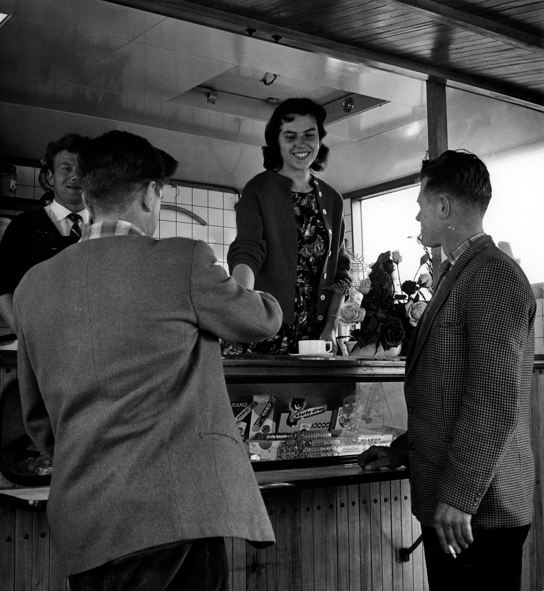 Twee heren - werkzaam in het Europort gebied - drinken een kop koffie bij de koffie kraam. De bevoorrading geschiedt door de firma R. Veugelers uit Rozenburg. In de vitrine van de kraam liggen zoetwaren, te weten rollen Rang en Venco drop. 1960.